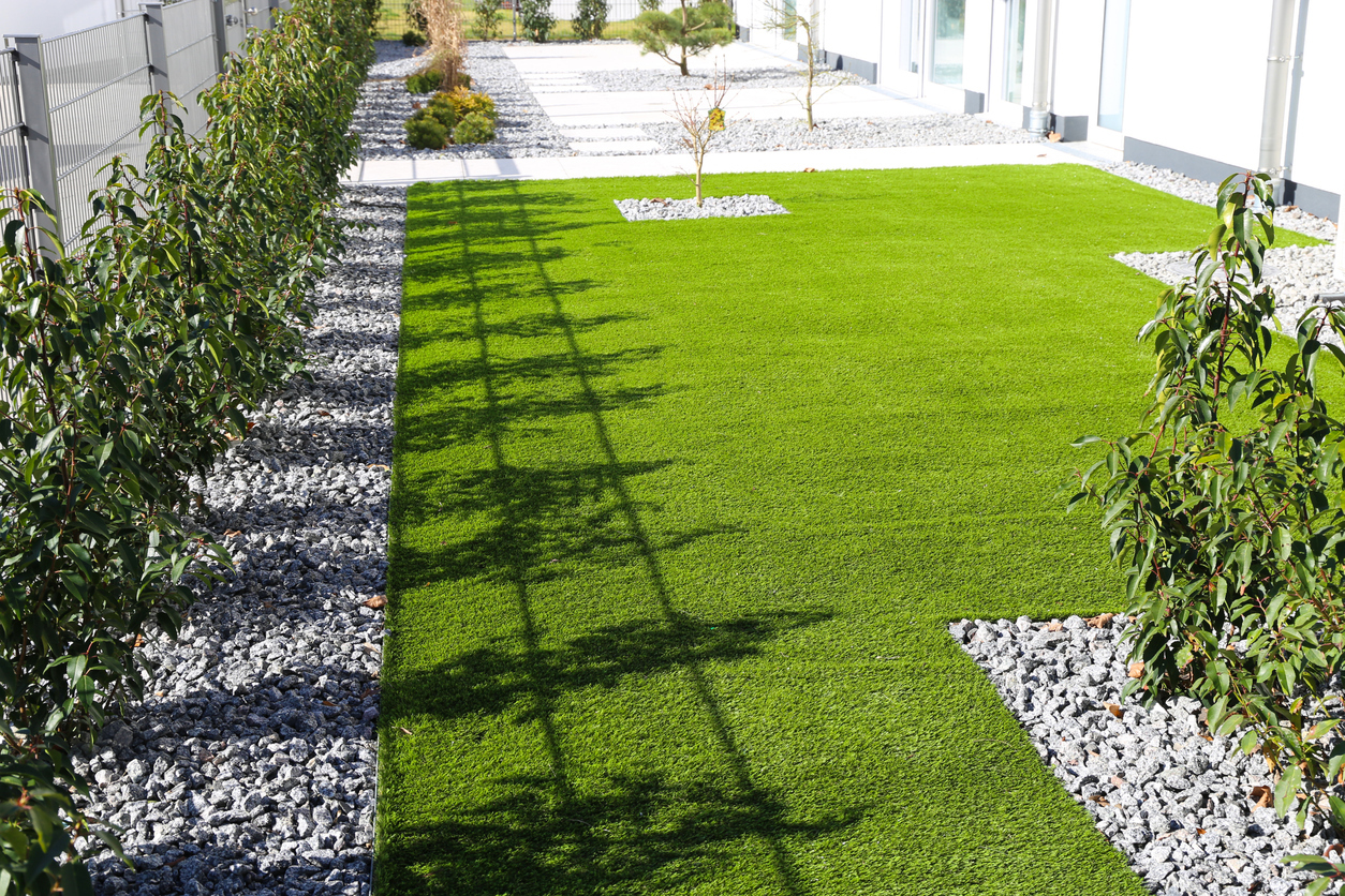 “Artificial grass backyard with modern landscaping, gravel borders, and young trees, offering a low-maintenance lawn solution for Calgary homes.
